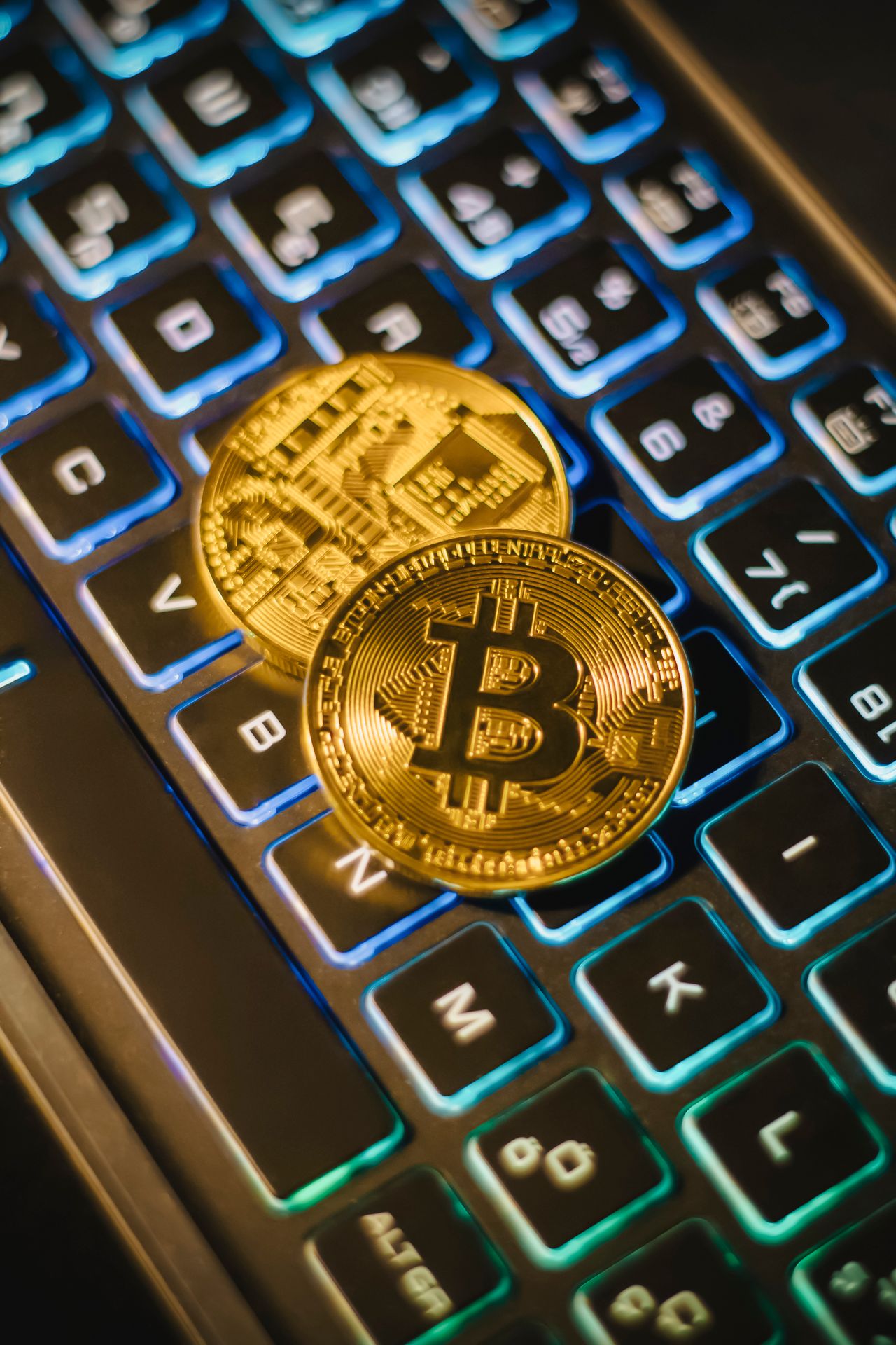two bitcoin coins resting on an illuminated keyboard, showing cryptocurrency and digital finance themes.
